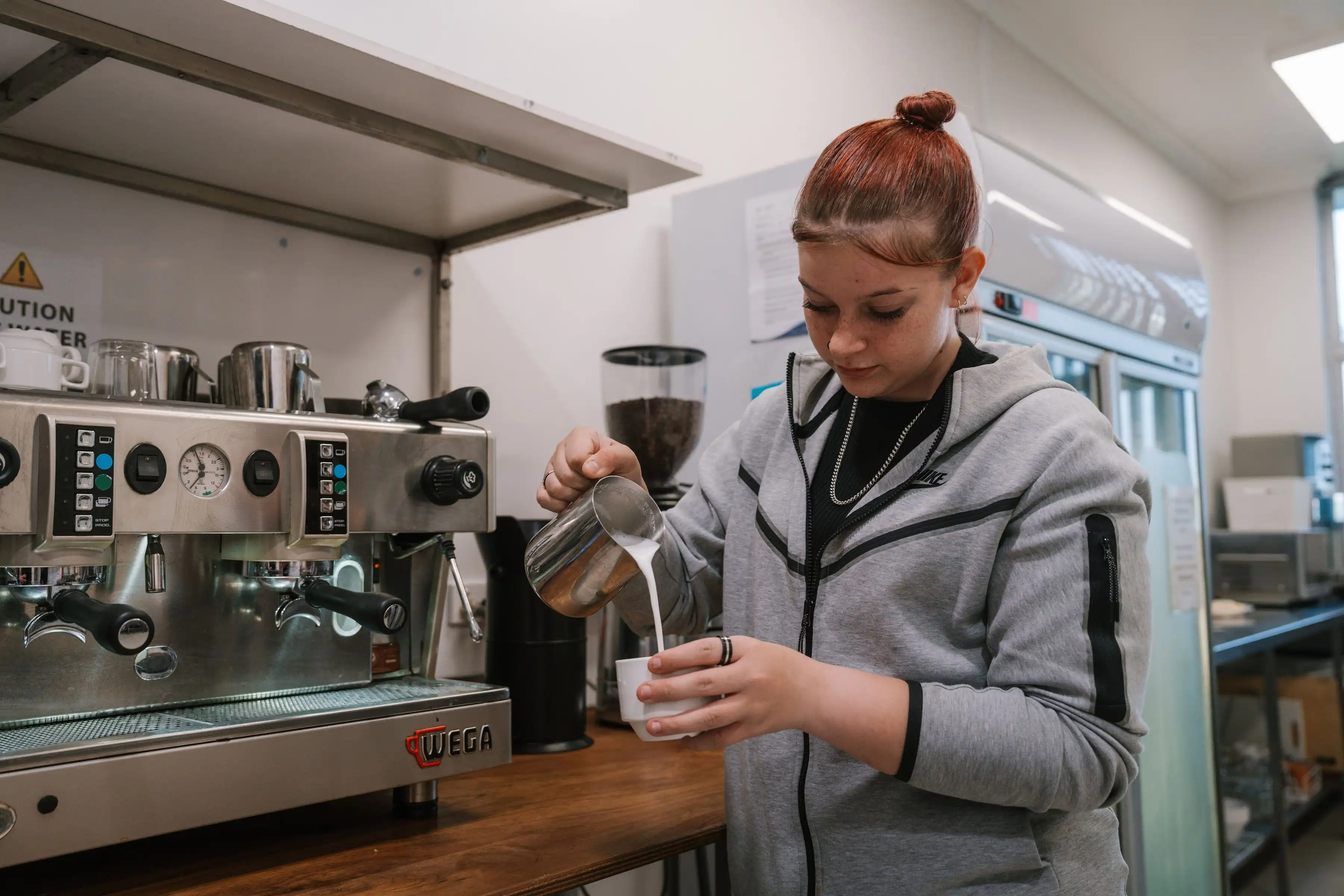 Barista pouring milk into coffee mug.